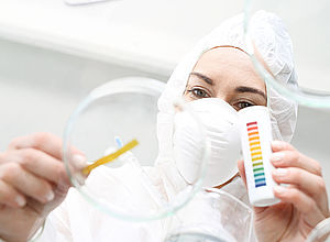 View from below of a lab technician with face mask holding a stripe of litmus into a petri dish | CWPharma - a project of Interreg Baltic Sea Region (photo: Panthermedia/Robert Przybysz)