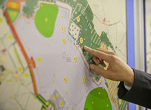 A hand pointing to a location on a map which is put up vertically.