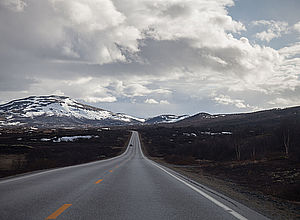 A distant view across a road into the snow-capped mountains, a single car coming in the distance to the viewer. | MAMBA - a project of Interreg Baltic Sea Region (photo: Oddleiv Apneseth)