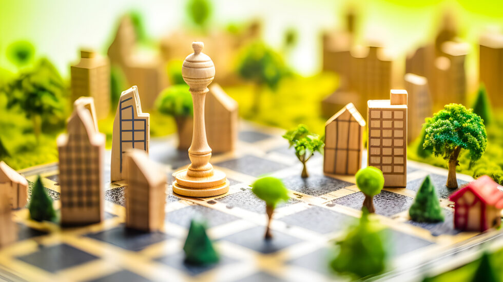Wooden chess piece resembling a queen standing on a checkered board surrounded by miniature wooden buildings and trees.