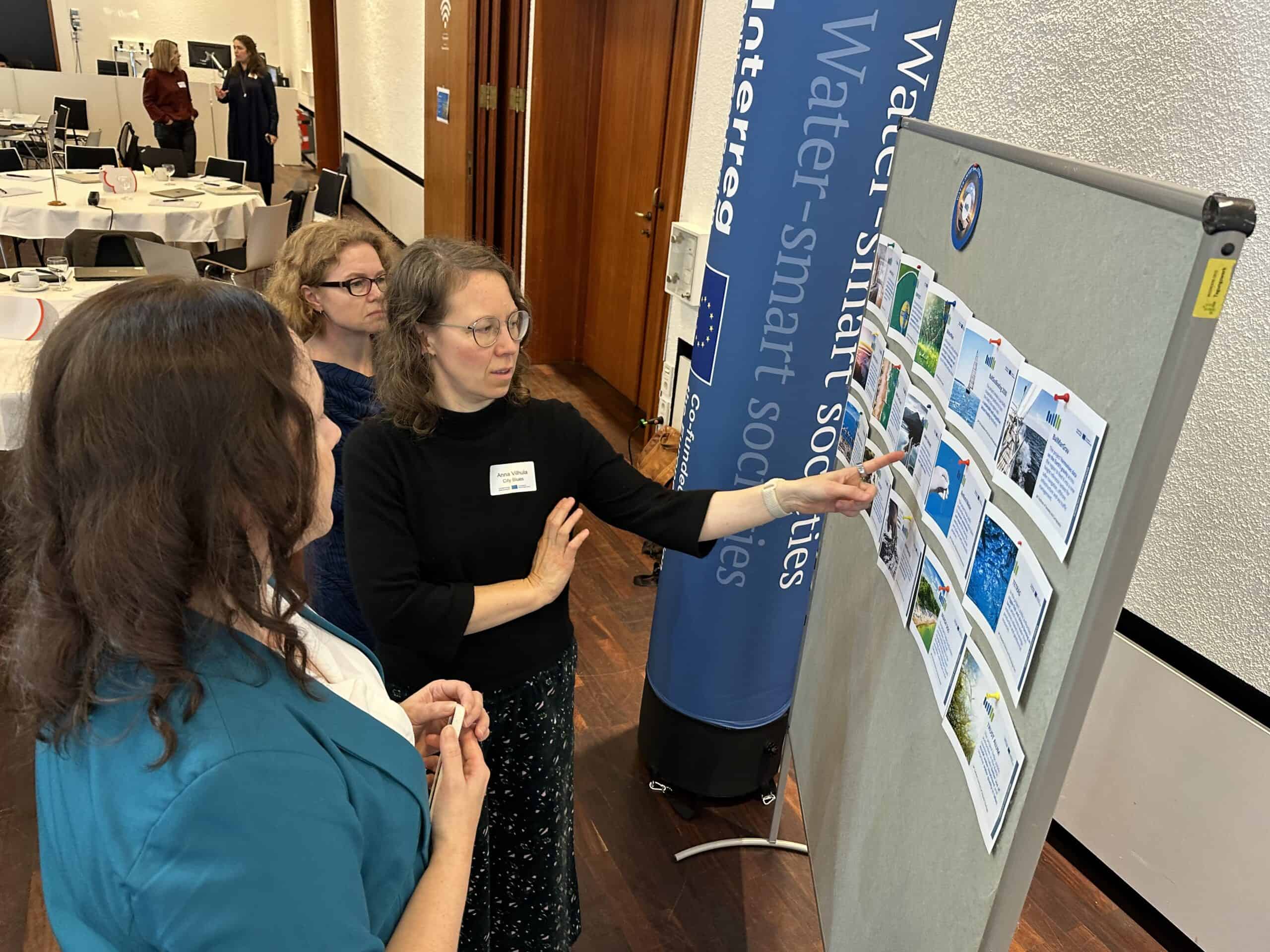 three persons interact by looking at the pinboard that contains project examples