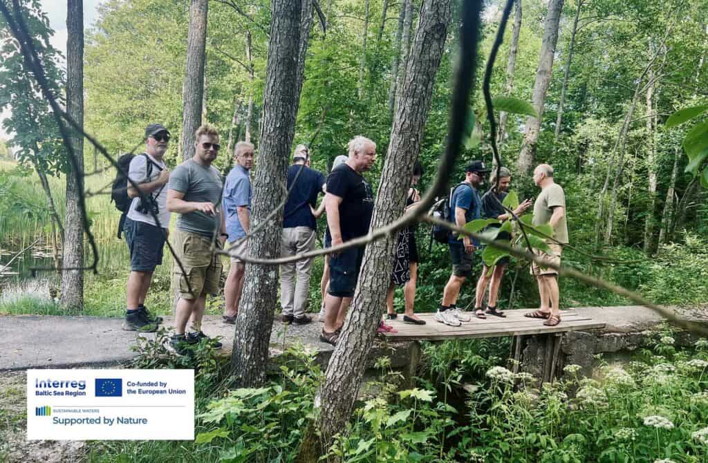 Eleven persons standing in the forest on a small bridge over water