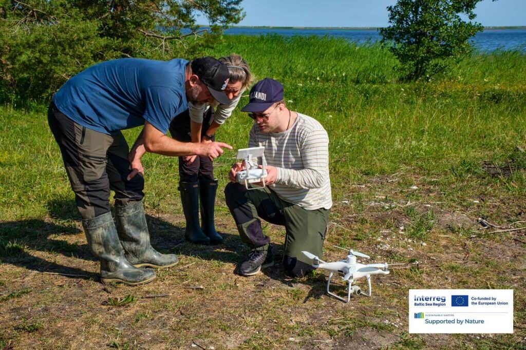 Three persons bending over and looking at a drone