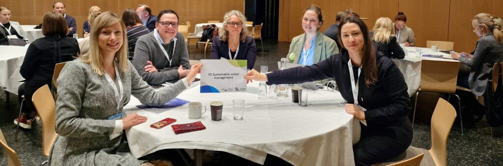 Representative of the GYPREG team sitting around a round table and holding a sign entitled "Sustainable water management".