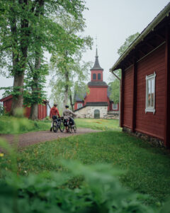 Two people walking their bikes, a church on the background