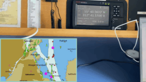 Navigation equipment showing vessel coordinates on a digital display and a nautical chart of the Copenhagen area with marked routes and symbols.