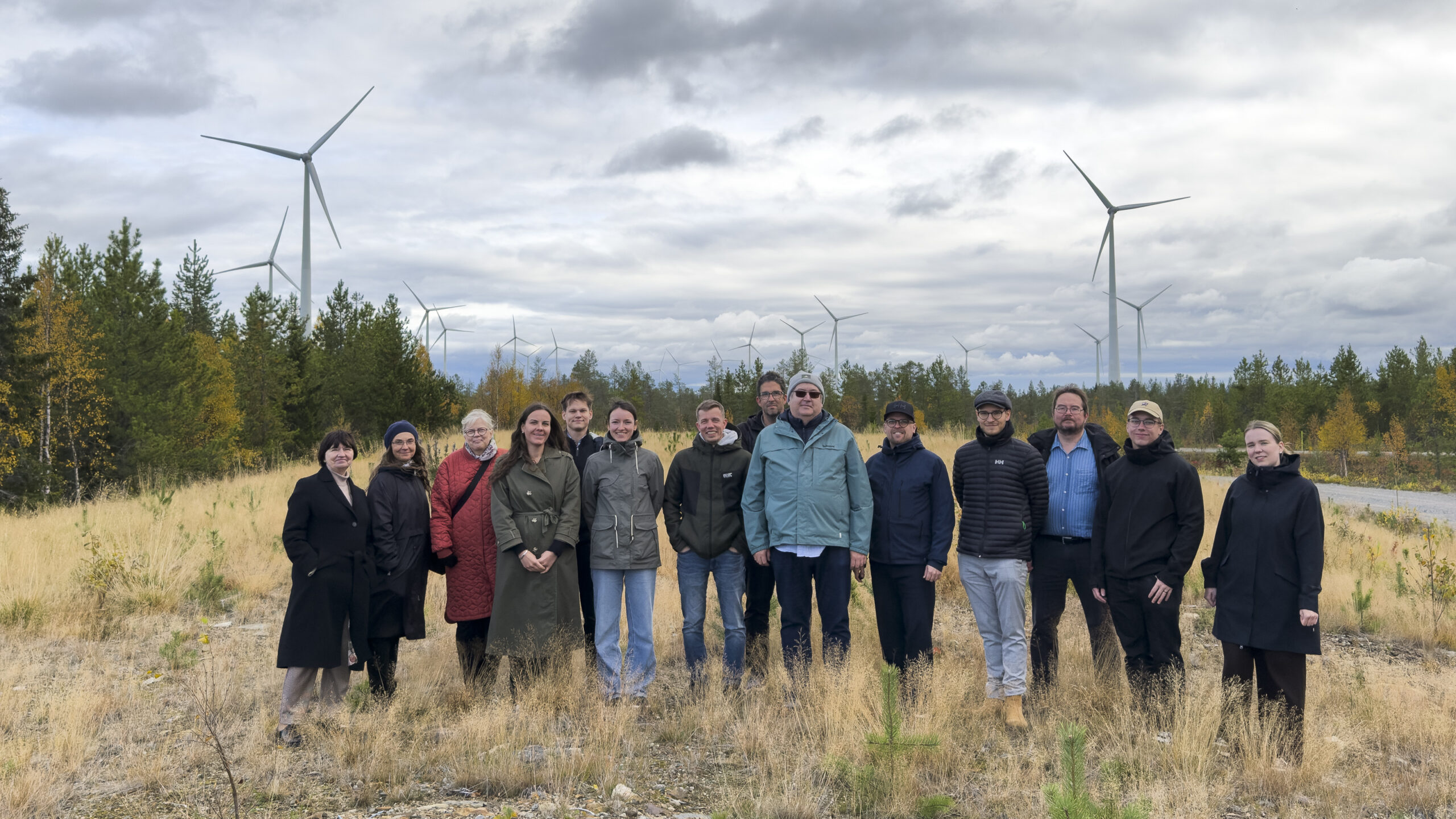 group photo with around 20 people standing on a field. In the backdround there are several wind power plants